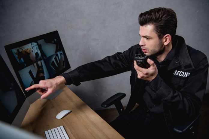 guard in uniform talking on walkie-talkie and looking at computer monitor